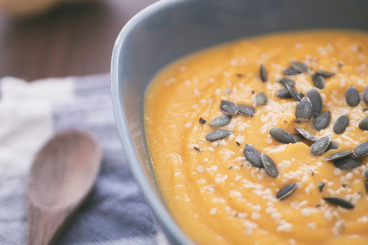 creamy pumpkin soup in light blue bowl with pepitas on top