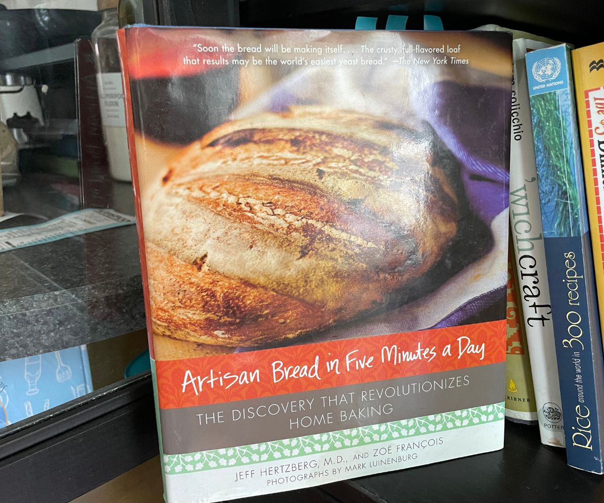 Artisan Bread in Five Minutes a Day standing in front of cookbook shelf in kitchen