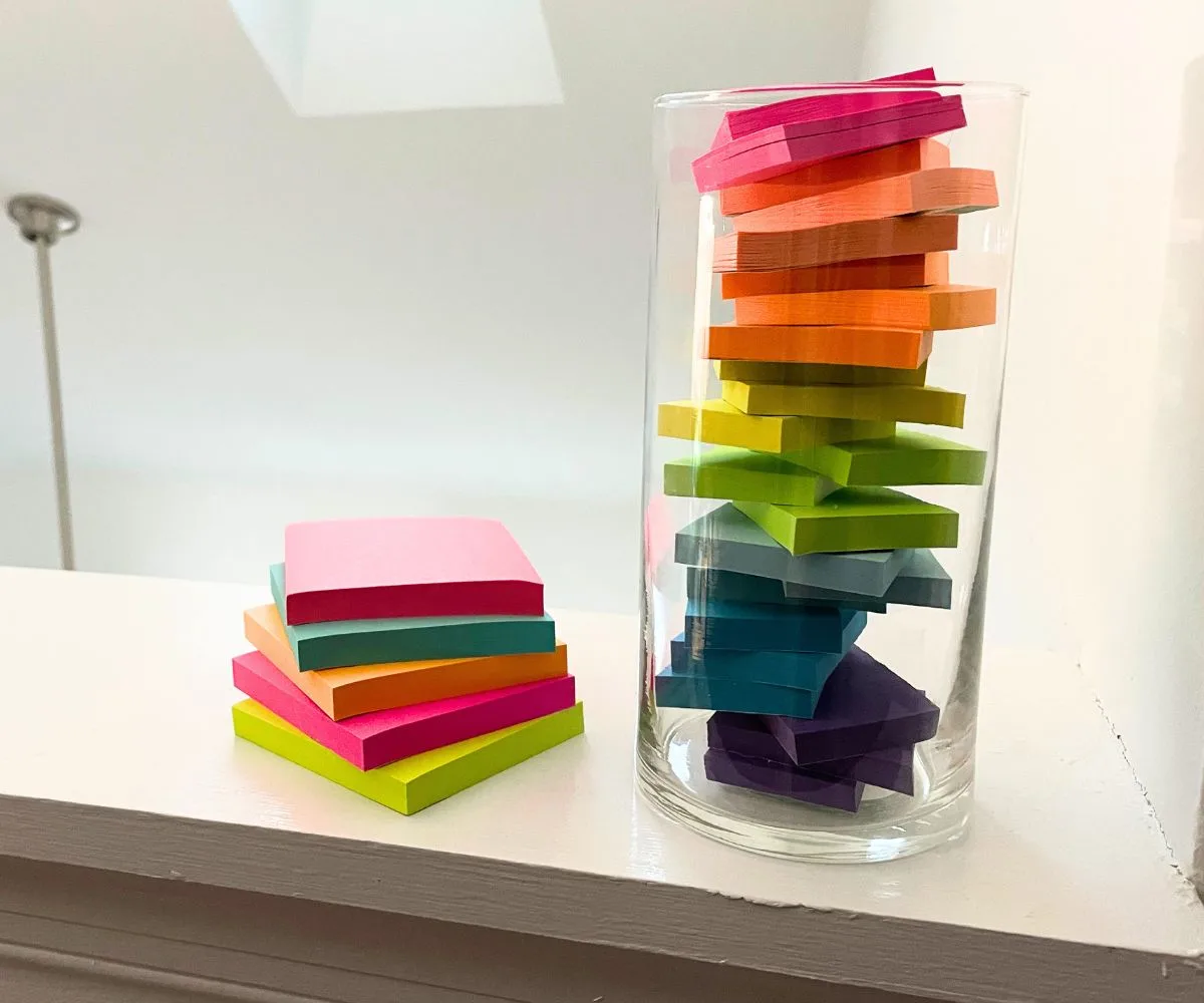 Two towers of post-it notes, one larger sized, and one smaller sized in a large glass vase