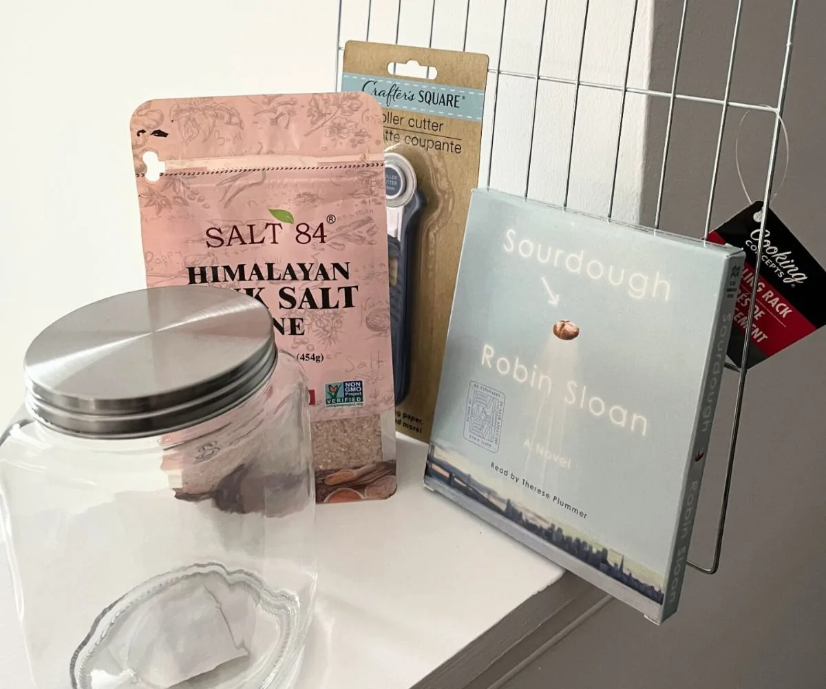 Himalayan sea salt bag, glass jar with lid, cooling rack, metal cutter, and Sourdough audiobook on white background