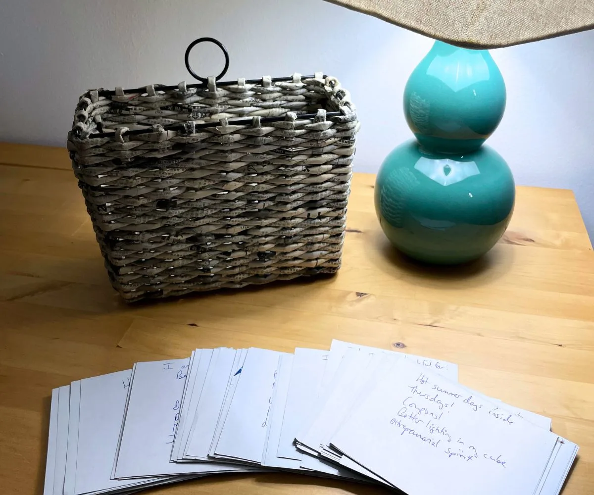 same newspaper basket with the backside of each calendar page showing the written gratitude lists on maple desk