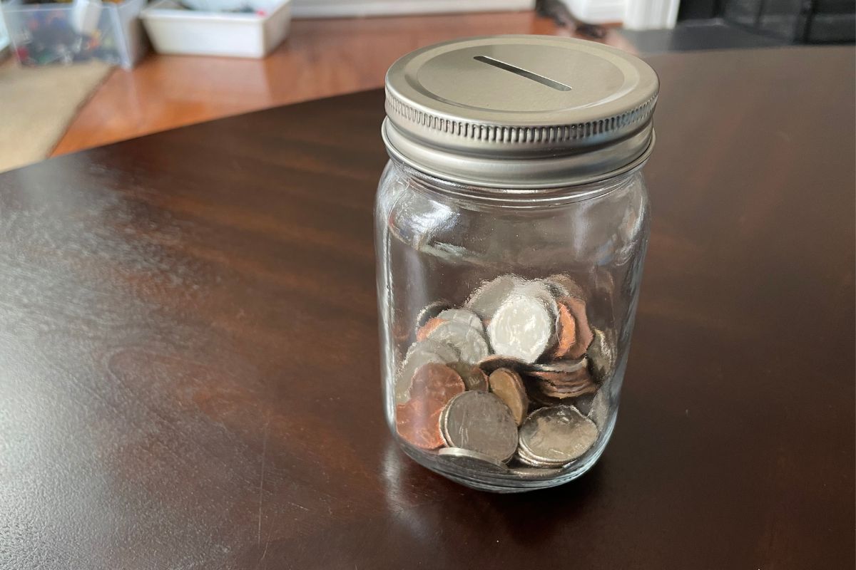 mason jar 1/3 filled with coins on dark table, with lid that has coin slot on it