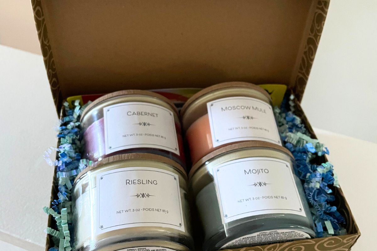 4 adult-drink scented glass candles with wooden tops in a gold box with confetti in it