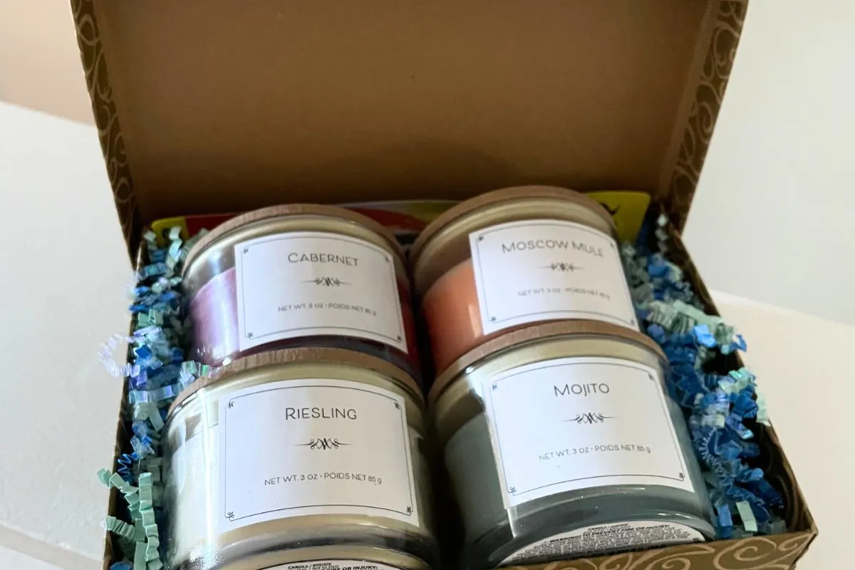 4 adult-drink scented glass candles with wooden tops in a gold box with confetti in it