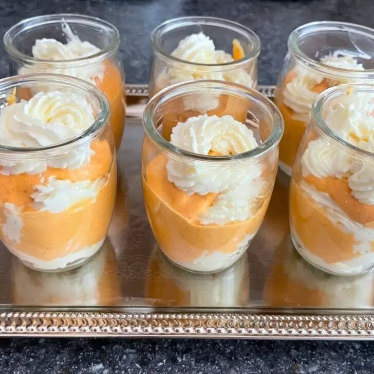 small roundish glasses of pumpkin cheesecake mousse glasses on silver tray