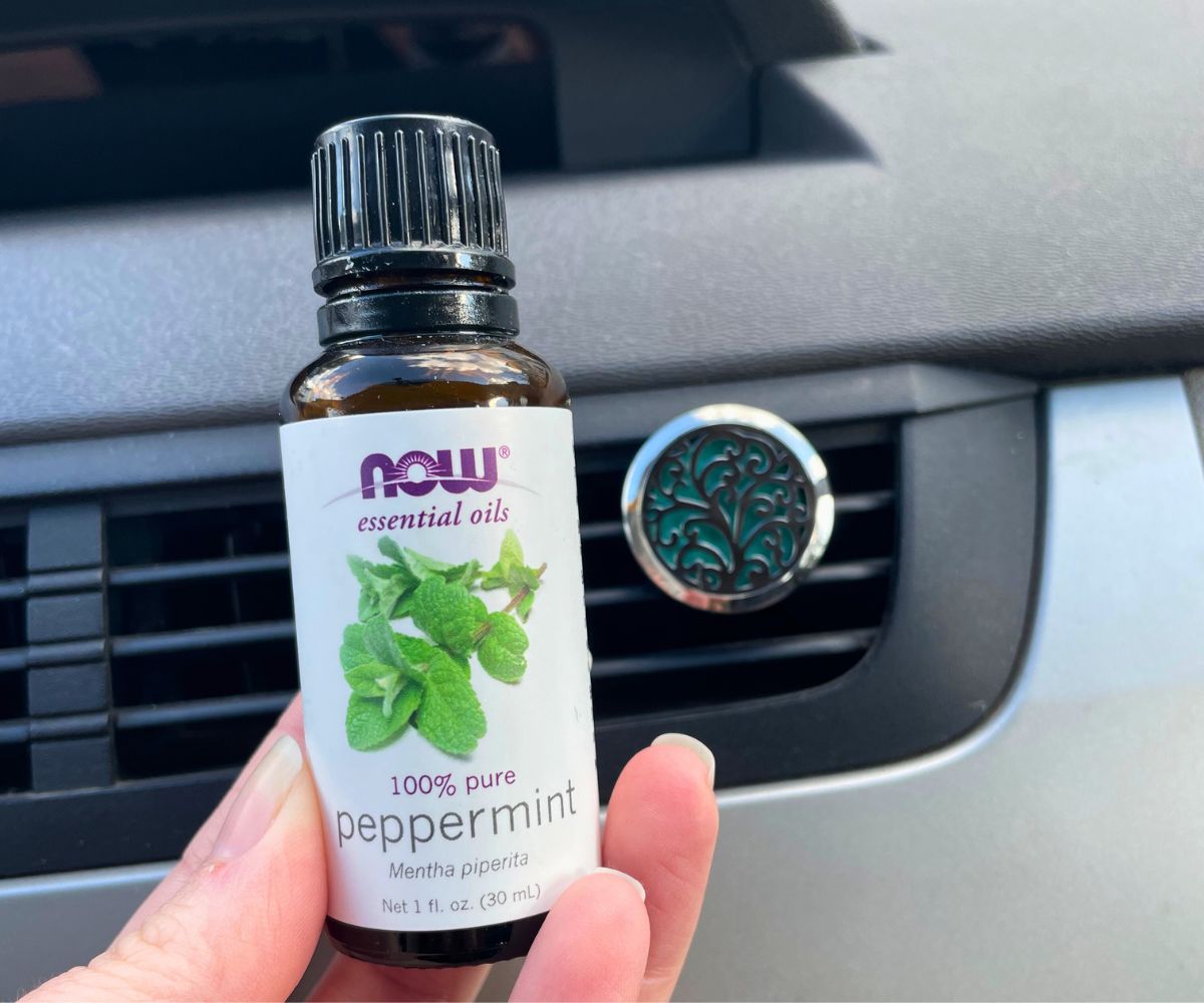 hand holding Peppermint 100% pure essential oil next to tree essential oil diffuser in car vent