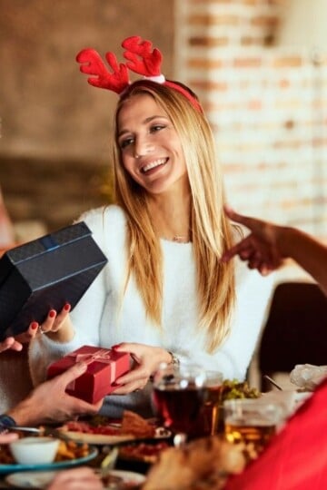three women in Santa hats exchanging Secret Santa gifts with $20 maximum
