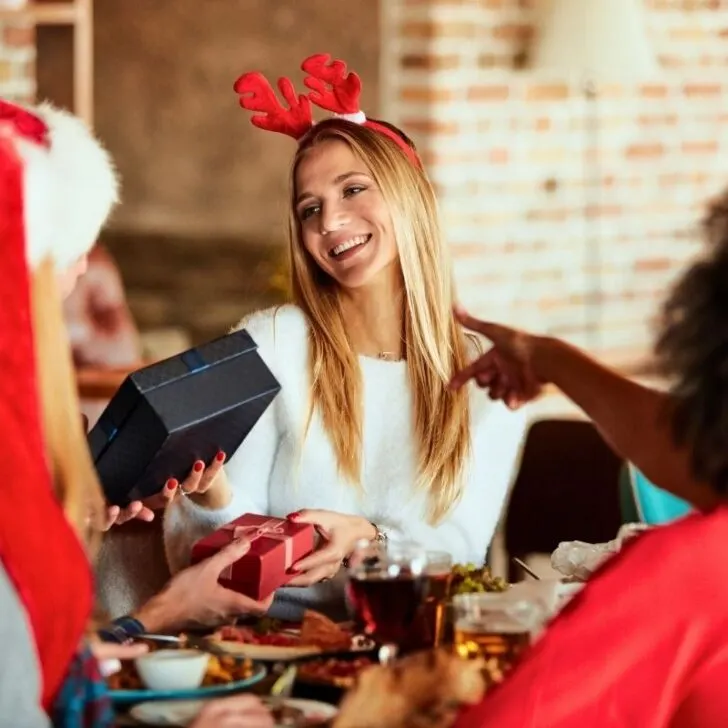 three women in Santa hats exchanging Secret Santa gifts with $20 maximum