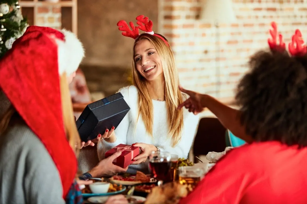 three women in Santa hats exchanging Secret Santa gifts with $20 maximum