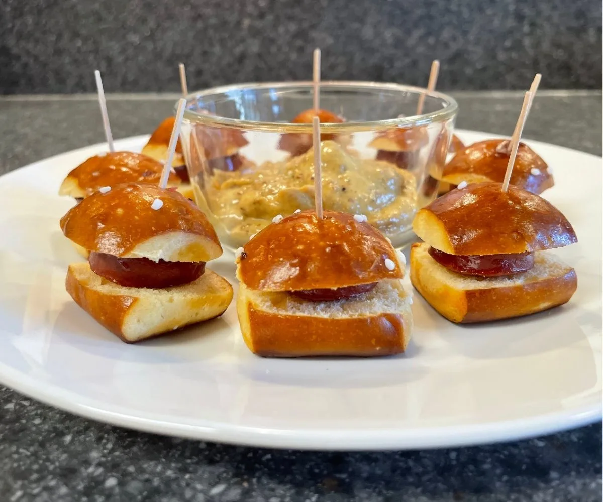 pretzel sausage bites with toothpicks through them and a dipping mustard in middle of plate