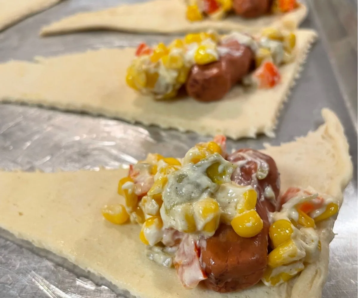 Inside of crescent rolls before baked with mini hot dog and spoonful of hot corn chile dip