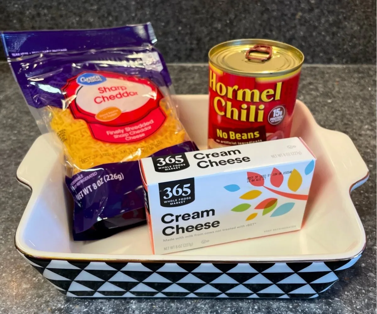 oven safe dish with hormel chili can, cream cheese package, and shredded cheese container sitting inside