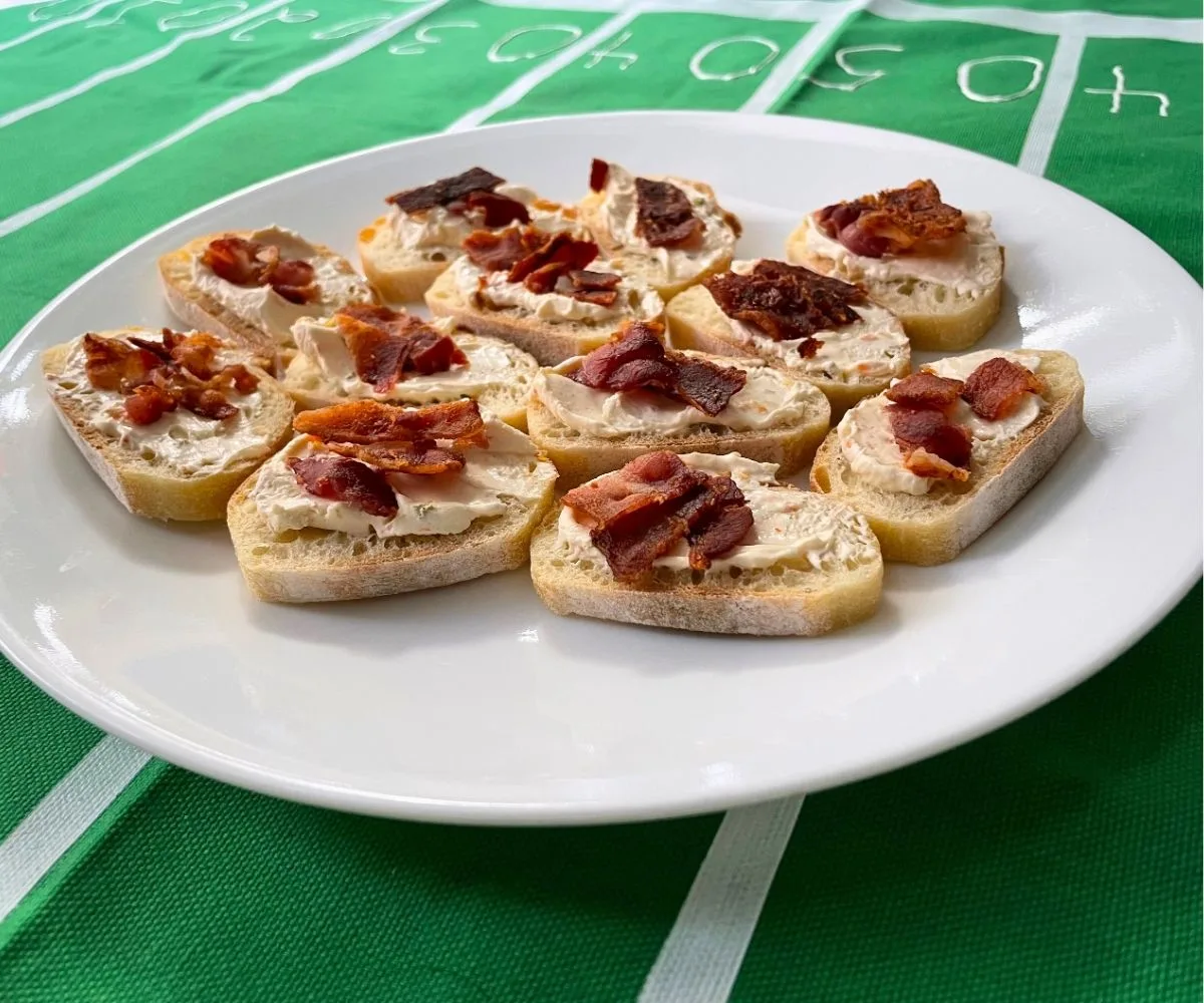 plate full of bacon vegetable cream cheese crostinis on homemade football field tablecloth