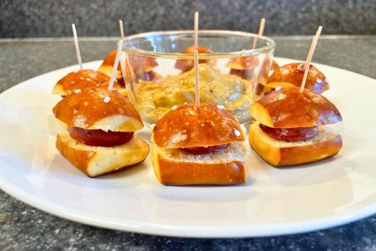 white plate of pretzel sausage bites with toothpicks and mustard sauce
