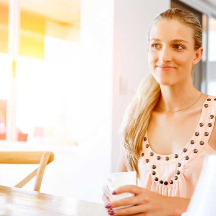 woman with coffee smiling, wearing peachy top