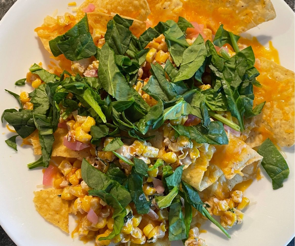 white plate full of nachos with lots of green spinach, corn, onions, etc. 