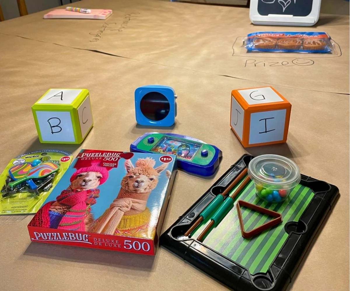 pile of mini games and dice with letters written on them, plus a timer on table wrapped in butcher paper