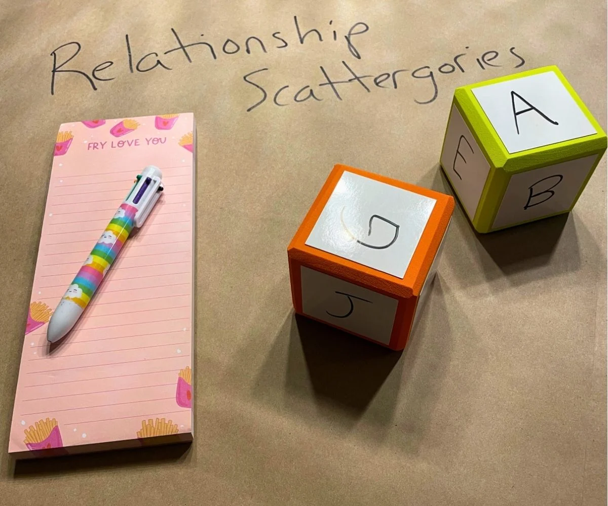 two large dice with letters of alphabet written on them, pad of paper and a pen, under "Relationship Scattergories" written in marker