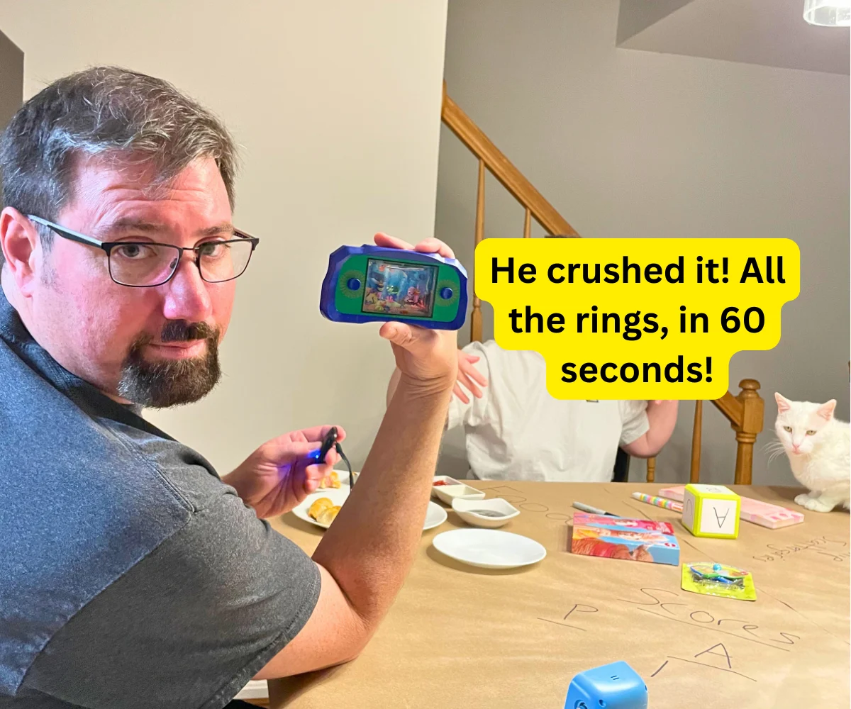 husband, proud, holding up his winning handheld water game, text overlay "he crushed it! All the rings, in 60 seconds!"