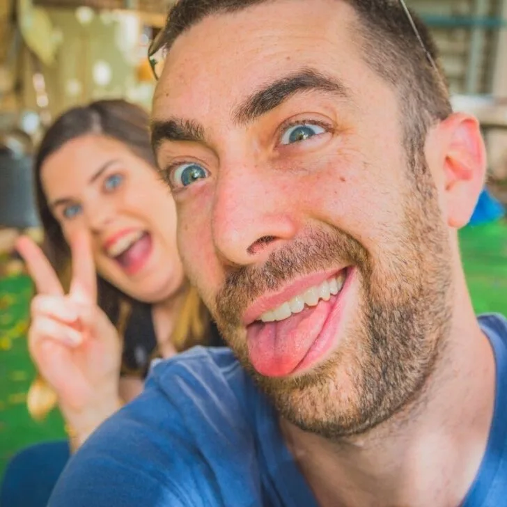 man with tongue out and woman giving peace sign having so much fun together