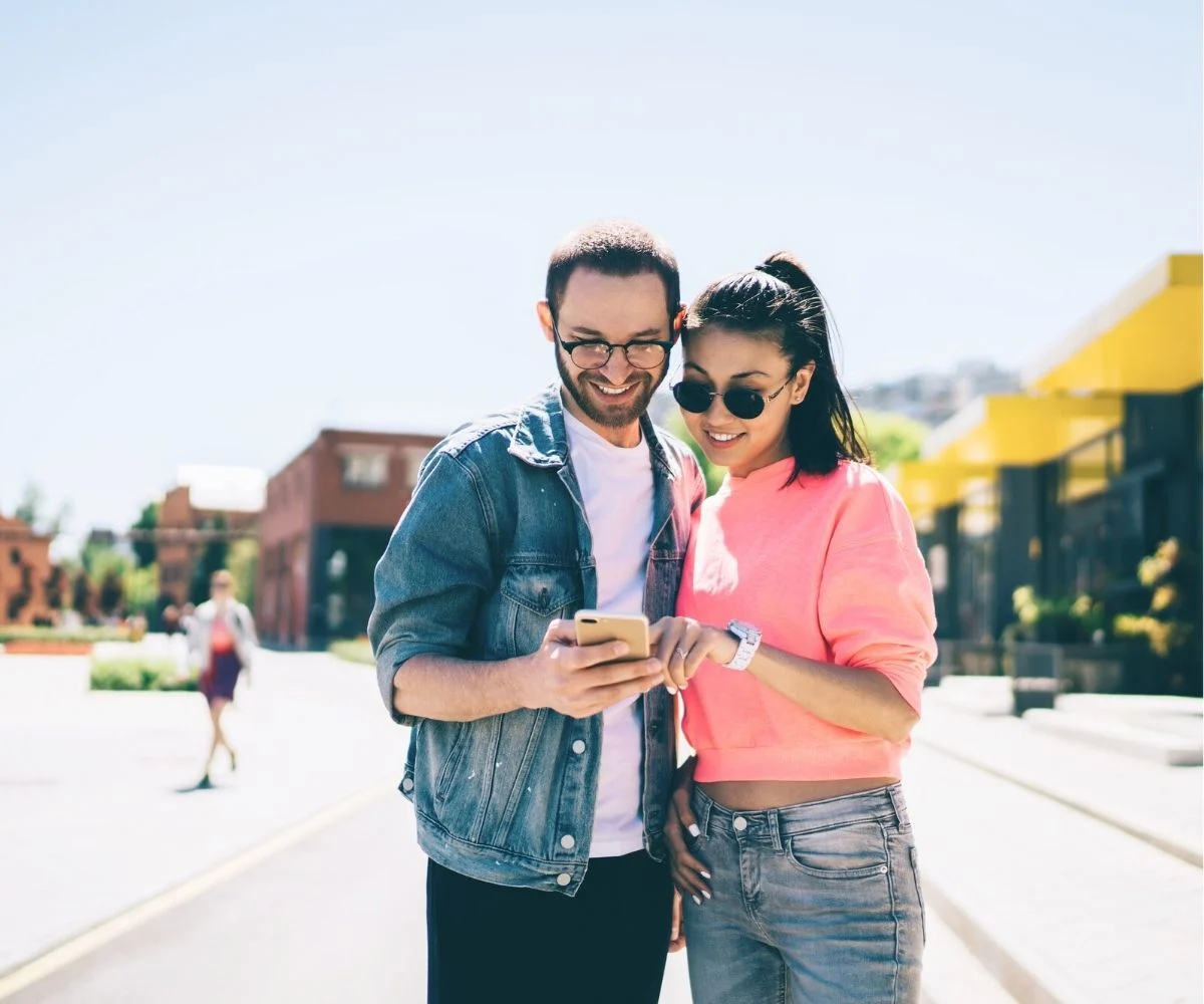 couple smiling pointing at smartphone out on the town