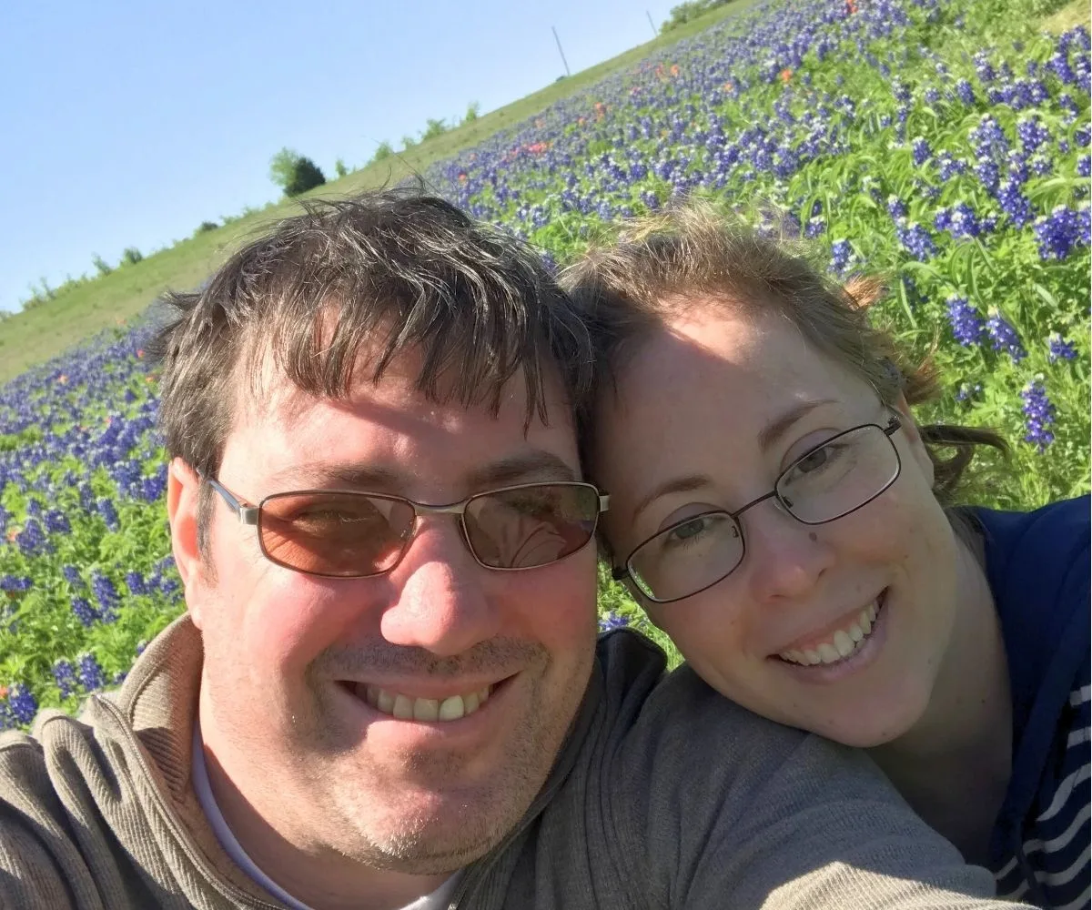 author and husband smiling in camera with blue bonnets all around them
