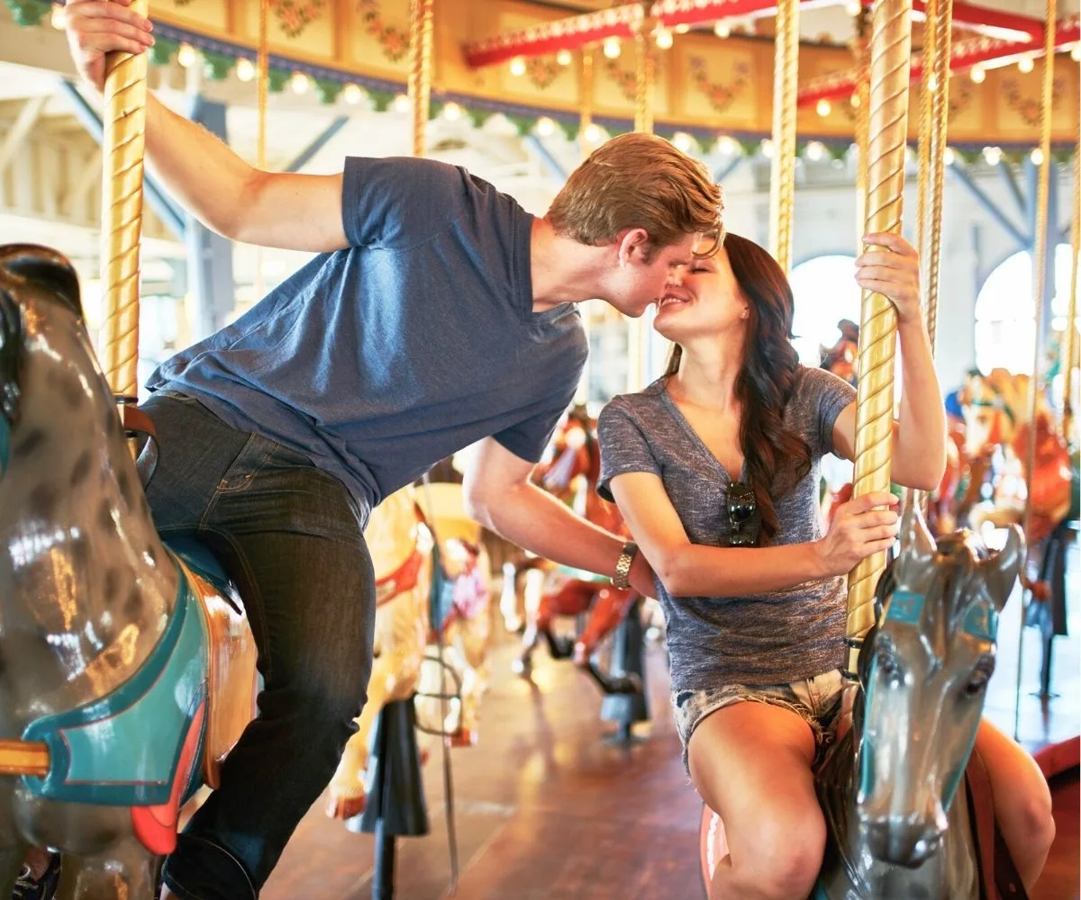 couple riding separate horses on carousel, kissing and smiling
