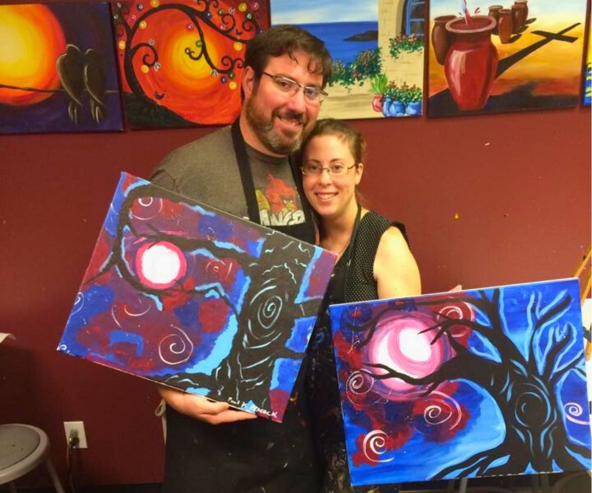 husband and wife showing off paintings from paint date night