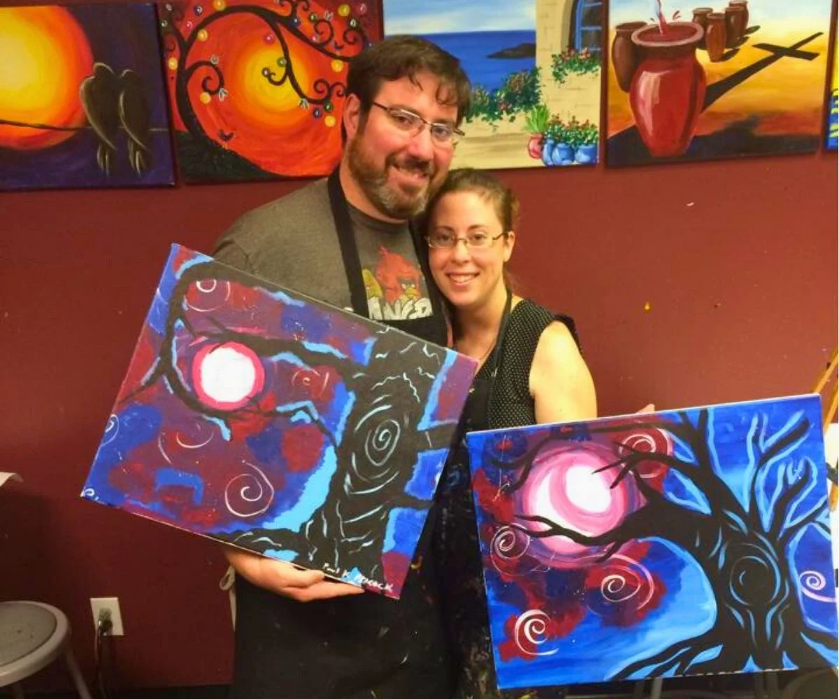 husband and wife showing off paintings from paint date night