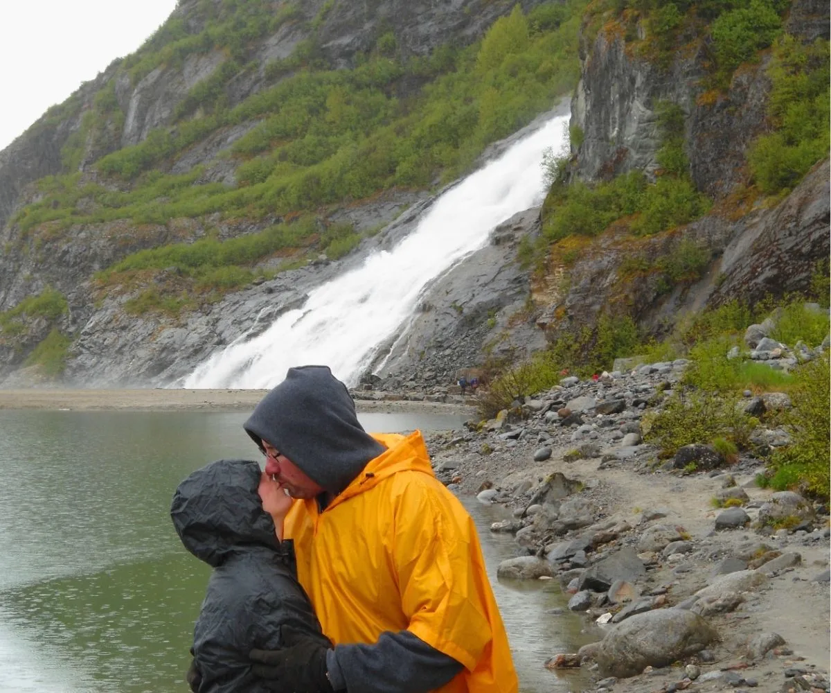 husband and wife kissing in front of a waterfall they hiked to