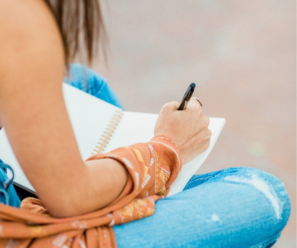 woman in jeans writing a burn list in a notebook