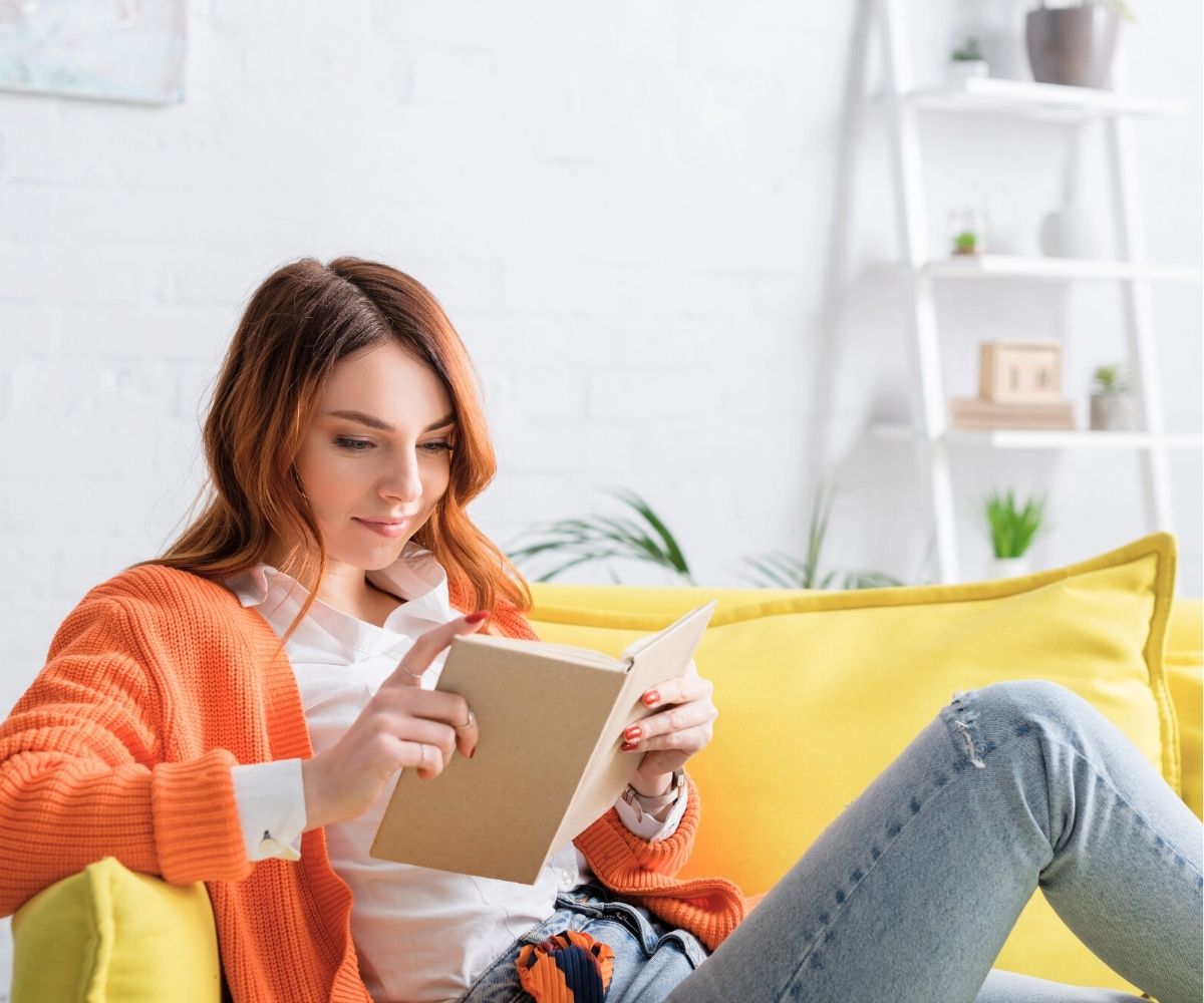 girl in sweater on bright yellow sofa reading