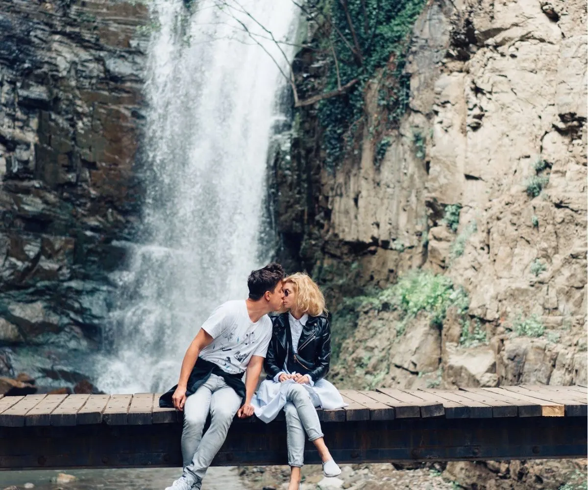 couple on wooden bridge kissing each other in front of waterfall
