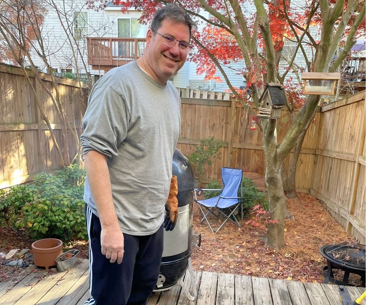 husband smiling, smoking meat on back patio with wife