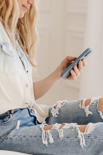 woman on phone on bed, wearing trendy jeans
