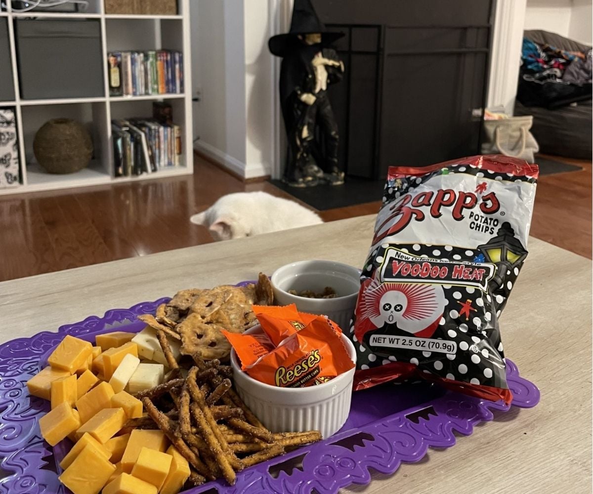 dark purple food board filled with Halloween-themed snacks and candies with vampire in background