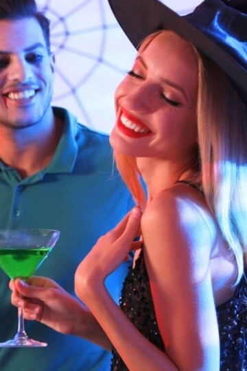 couple in witch hat and vampire makeup at home with Halloween beverages
