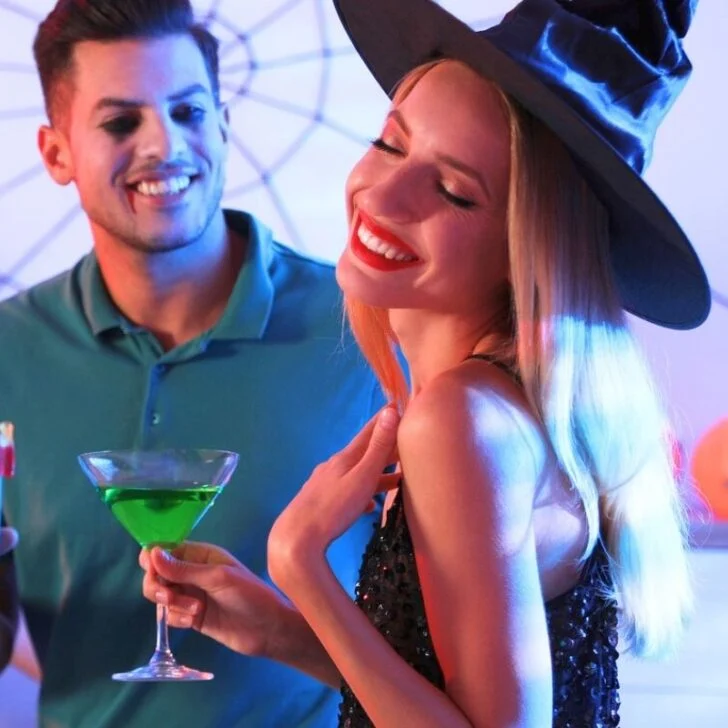 couple in witch hat and vampire makeup at home with Halloween beverages