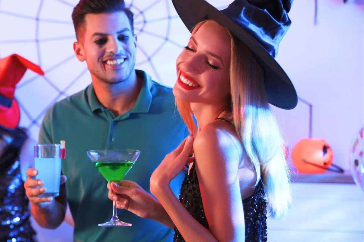 couple in witch hat and vampire makeup at home with Halloween beverages