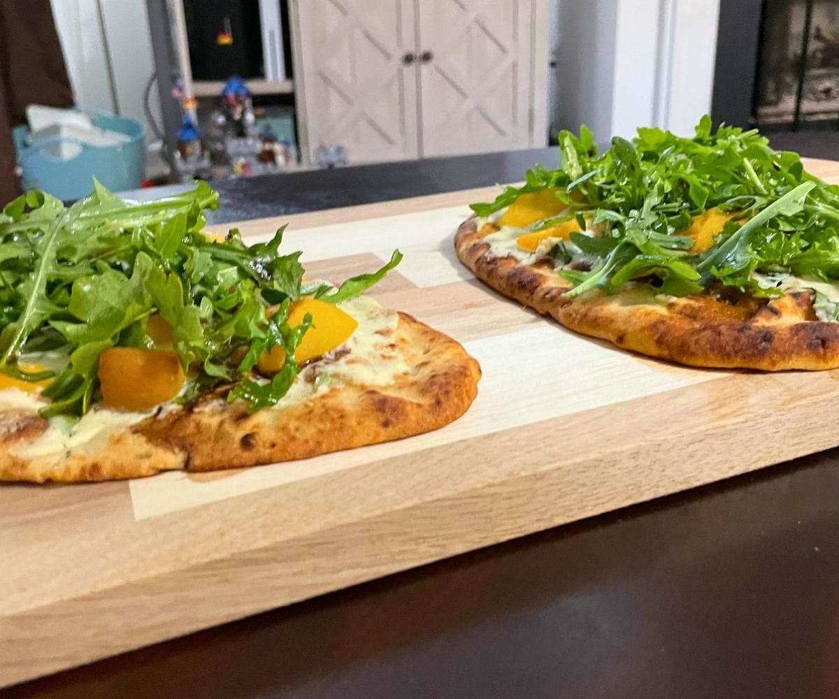 two colorful mini naan pizzas on a light wooden board