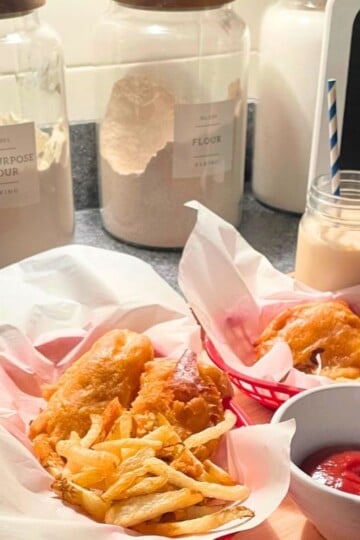 beautiful fish and chips in red baskets and milkshakes on light wooden tray with menu chalkboard sign