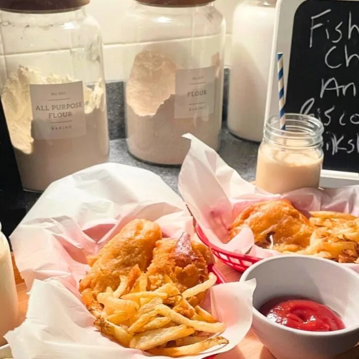 beautiful fish and chips in red baskets and milkshakes on light wooden tray with menu chalkboard sign