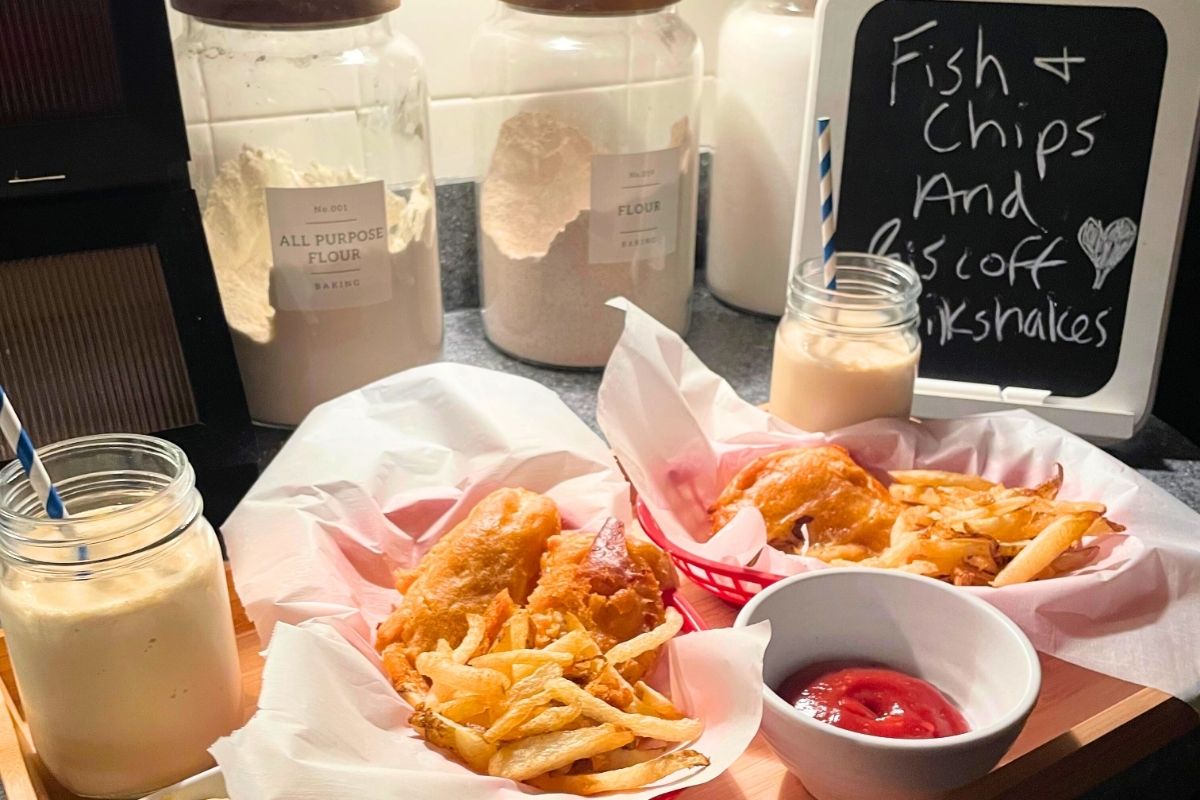 beautiful fish and chips in red baskets and milkshakes on light wooden tray with menu chalkboard sign