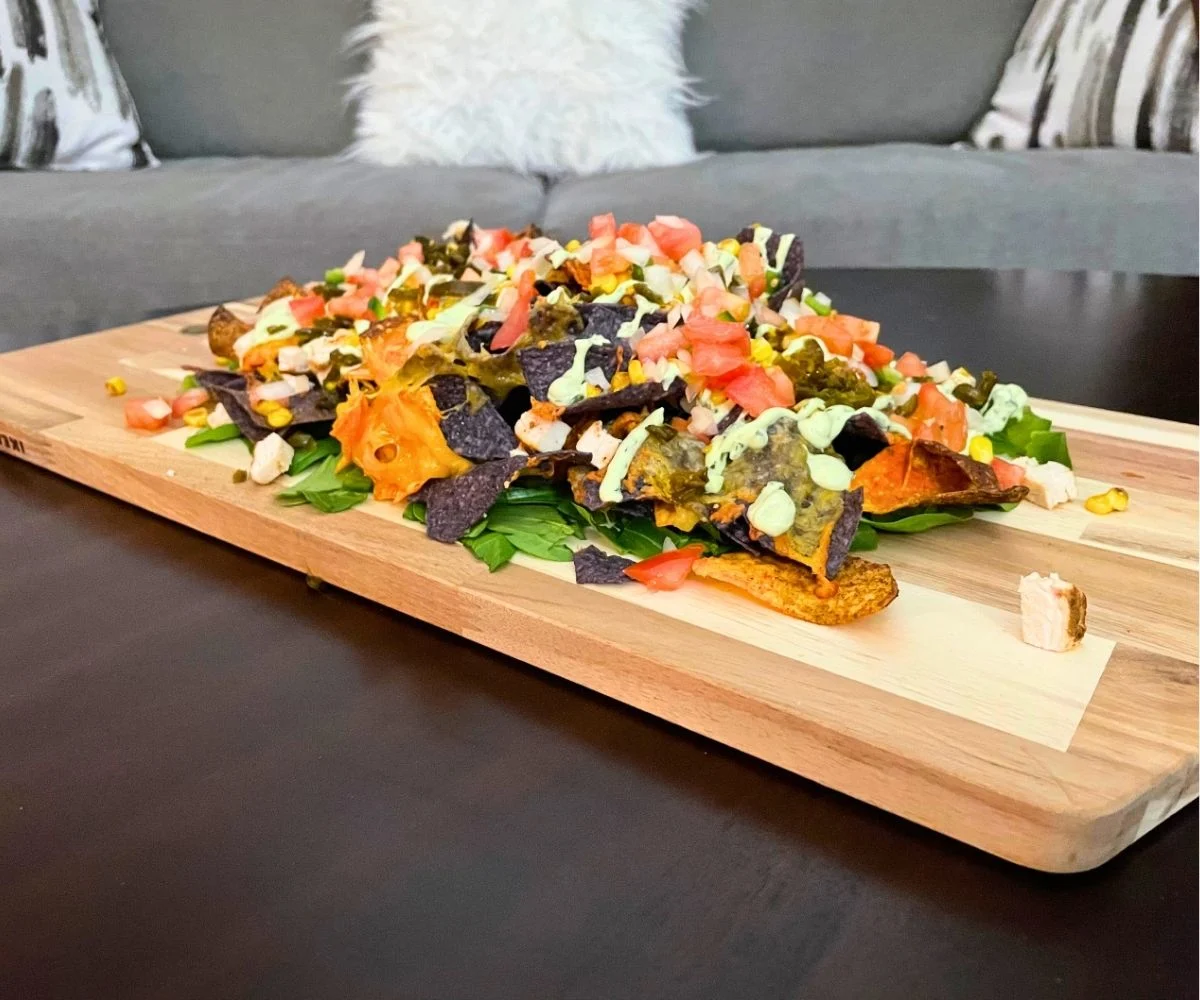 giant light wooden tray filled with a heap of colorful nachos on a dark wooden table, couch in background