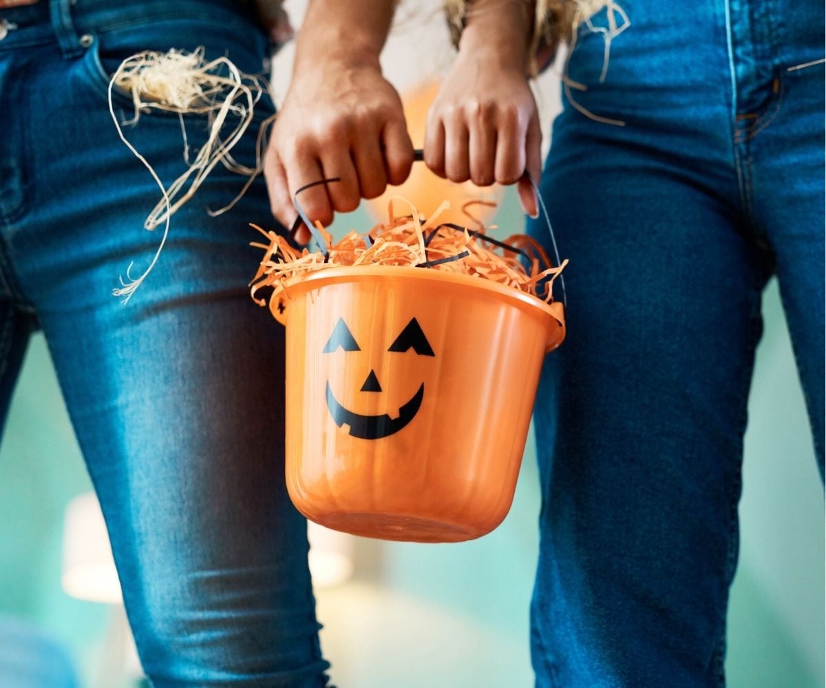 couple in jeans holding onto pumpkin pail of treats together