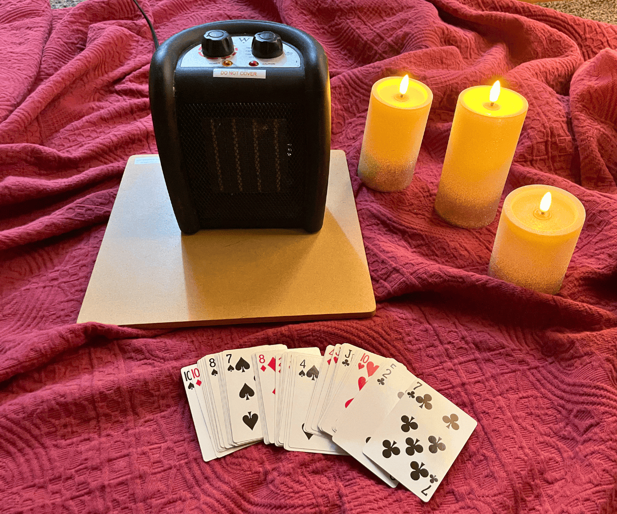 red blanket, with battery candles, deck of cards, and a space heater on top of wooden area