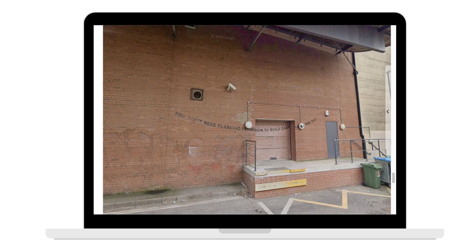 laptop with Banksy exhibit on red brick building