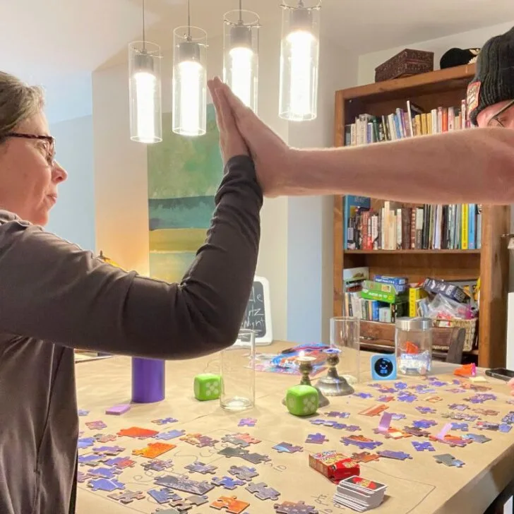 couple high fiving each other with tons of puzzle pieces on table