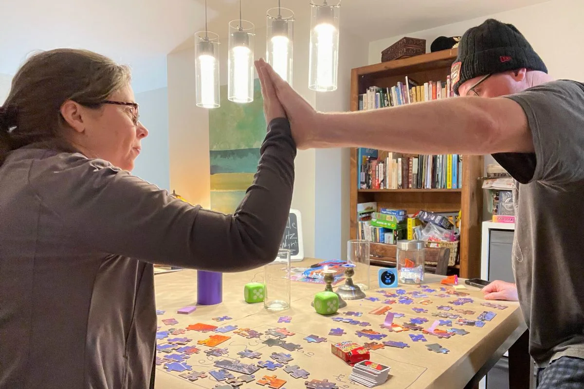 couple high fiving each other with tons of puzzle pieces on table