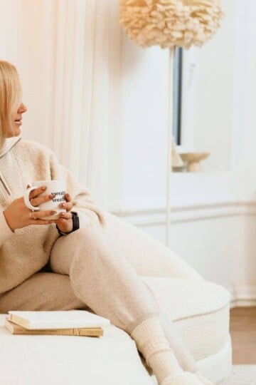 woman in neutral, lounging clothes on sofa with notebook and a mug